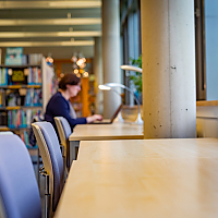 Arbeitsplätze entlang der Glasfront. Eine Frau im Hintergrund arbeitet an einem Laptop.