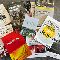 Grauer Tisch mit locker verteilten Büchern zu Geschichte, Politik und Gesellschaft, Cover sichtbar, teilweise überlappend, keine weiteren Gegenstände.