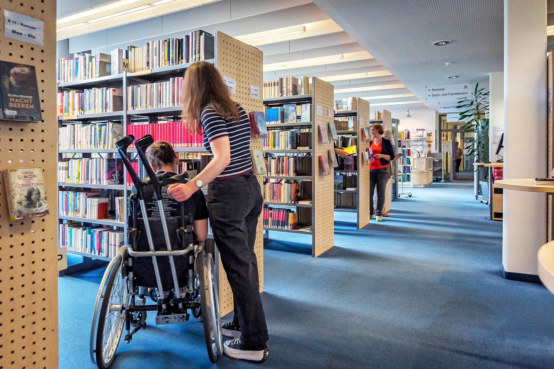Junge Frau sowie ein Rollstuhlfahrer vor einem Bücherregal